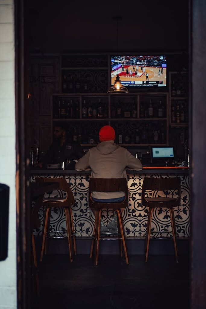 A person watching basketball on TV at a cozy bar with elegant decor.